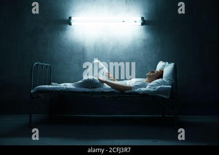 Psycho Mann im Bett liegend, dunkles Zimmer auf Hintergrund Stockfoto