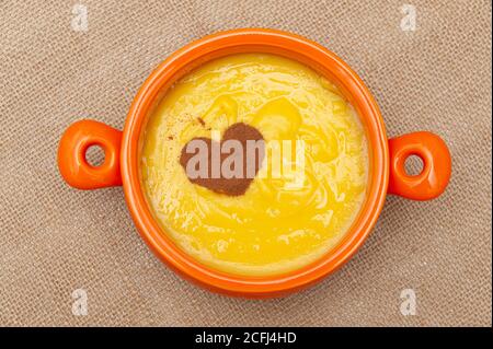 Hausgemachter süßer Maispudding in Brasilien als Curau oder Canjica Nordestina in Keramikschale bekannt. Zimtpulver in Herzform. Stockfoto