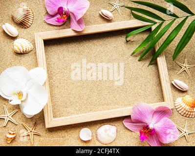 Sommer Strand Dekoration: Rahmen mit Orchideen, Muscheln und Seesterne auf Sand Hintergrund Stockfoto