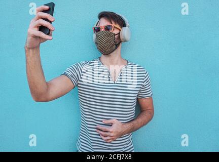 Kleiner Junge, der Selfie mit Gesichtsmask und Sonnenbrille im Bild nimmt Sommer - Teenager machen eine Videocall mit großen Kopfhörern an Zur Zeit des Coronavirus Stockfoto