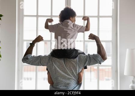 afroamerikanischer Vater mit kleinem Sohn auf Schultern mit Bizeps. Stockfoto