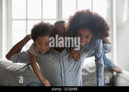 Junge starke afroamerikanische Papa trägt lachende Kinder. Stockfoto