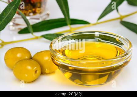 Olivenöl. Griechisches Olivenöl in durchsichtiger Glasschale mit Blättern und marinierten Oliven. Nahaufnahme, isoliert auf weißem Hintergrund. Stockfoto