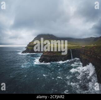 Luftdrohnenpanorama von Gasadalur Dorf und Mulafossur seinen ikonischen Wasserfall, Vagar, Färöer Inseln, Dänemark. Raue See im nordatlantik Ozean Stockfoto