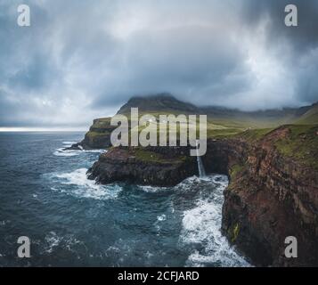 Luftdrohnenpanorama von Gasadalur Dorf und Mulafossur seinen ikonischen Wasserfall, Vagar, Färöer Inseln, Dänemark. Raue See im nordatlantik Ozean Stockfoto