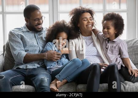 Glücklich gemischtes Rennpaar Eltern entspannen auf dem Sofa mit Kindern. Stockfoto