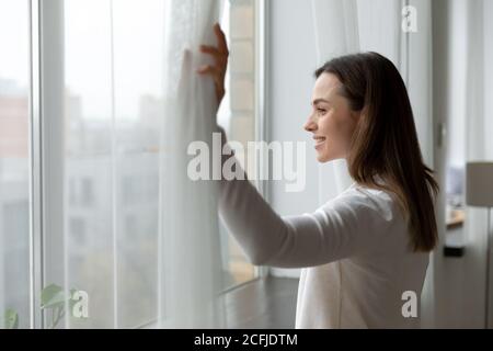 Seitenansicht glücklich attraktive Frau öffnen Vorhänge. Stockfoto