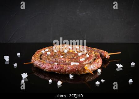 Gegrillte Spiralwurst mit Salz isoliert auf dunklem Hintergrund Stockfoto