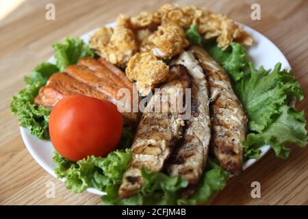 Drei Arten von Fisch auf einem Salat mit Tomaten. Köstlicher Meeresfisch in Cornflakes gebraten Stockfoto