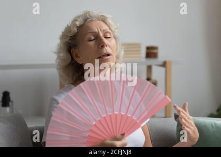 Erschöpft überhitzt reife Frau winkende Ventilator, sitzt auf der Couch Stockfoto