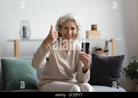 Überglücklich zufrieden mittleren Alters Frau zeigt Daumen nach oben, halten Smartphone Stockfoto