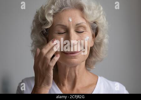 Close up Zufriedene Frau mittleren Alters Anwendung feuchtigkeitsspendende Gesichtscreme Stockfoto