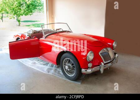 Schöner Top Down Sportwagen in leuchtendem Rot auf einem Plastikplanen in jemandes Garage, die sehr geliebt worden ist Stockfoto