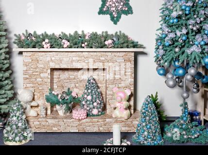 In der Nähe des beigen Steinkamins gibt es Geschenke, dekorative Weihnachtsbäume, Spielzeug, Bälle und Fichtenzweige in grünen Perltönen, Stockfoto