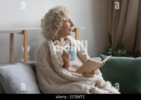 Verträumte Frau mittleren Alters gewickelt warme Decke zu Hause entspannen Stockfoto