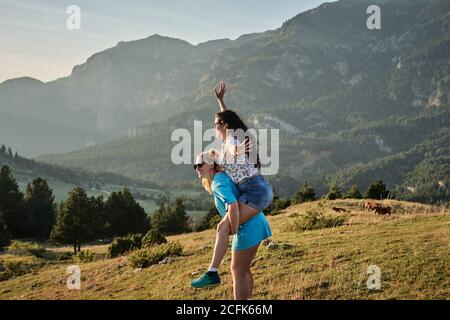 Seitenansicht der unbeschwerten Frau Huckepack Freundin auf dem Hintergrund der majestätischen Hochlandlandschaft im Sommer Stockfoto