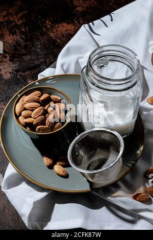 Schüssel mit natürlichen Mandeln in der Nähe Glas Glas von frisch platziert Vegane Milch auf Teller und Serviette im dunklen Raum Stockfoto