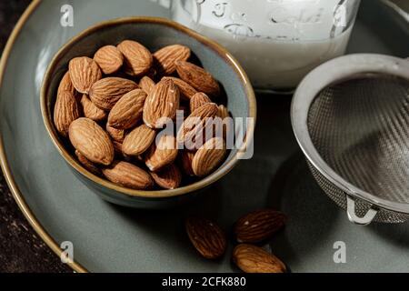 Von oben Keramikschale mit frischen Mandeln auf den Teller gelegt In der Nähe Flasche vegane Milch und Sieb Stockfoto