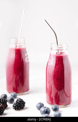 Beere Smoothie auf Glasflaschen auf weißer Marmoroberfläche. Vertikales Bild. Stockfoto