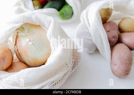 Nahaufnahme von Rohkartoffeln und Zwiebeln in umweltfreundlichem Gewebe Taschen auf dem Tisch in der Küche platziert Stockfoto