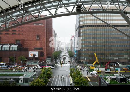 Fukuoka, Japan - Finanzgebäude in Hakata Station Geschäftsviertel. Hauptstraße im Bau. Vielbeschäftigte Passagiere mit Regenschirm an einem regnerischen Tag. Stockfoto