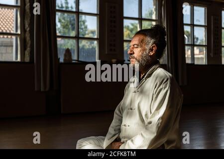 Ernte der Seitenansicht des fokussierten bärtigen ethnischen älteren Mannes Chi-Kung-Meditation in Lotusposition im dunklen Studio üben Stockfoto