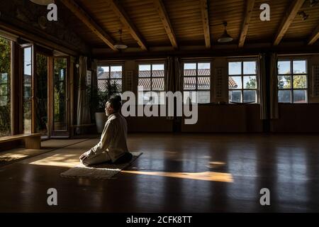 Ganzkörper-Seitenansicht des fokussierten bärtigen ethnischen älteren Mannes Chi-Kung-Meditation in Lotusposition im dunklen Studio üben Stockfoto