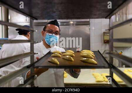 Männlicher Koch trägt Uniform und medizinische Maske Vorbereitung leckere Gebäck In der Küche der Bäckerei während der Coronavirus-Epidemie Stockfoto