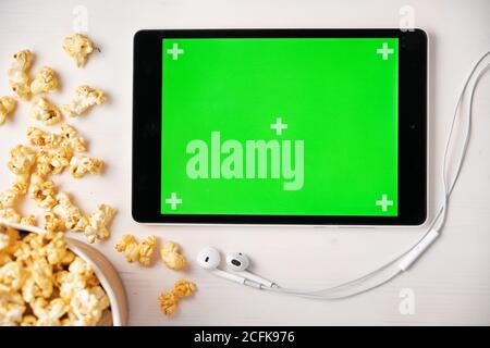 Tablet mit Chroma-Key, Popcorn-Box und Apple-Kopfhörer auf dem weißen Tisch. Platz für Werbung und Logo. Stockfoto