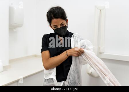 Ärztin, die Schutzanzug mit Gesichtsmaske aufsetzt Während der Vorbereitung auf die Arbeit während der Coronavirus-Pandemie Stockfoto