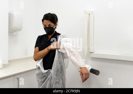 Ärztin, die Schutzanzug mit Gesichtsmaske aufsetzt Während der Vorbereitung auf die Arbeit während der Coronavirus-Pandemie Stockfoto