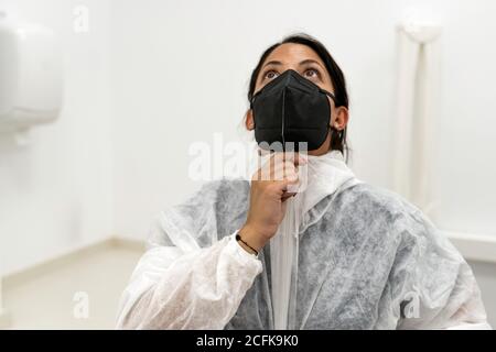 Ärztin, die Schutzanzug mit Gesichtsmaske aufsetzt Während der Vorbereitung auf die Arbeit während der Coronavirus-Pandemie Stockfoto