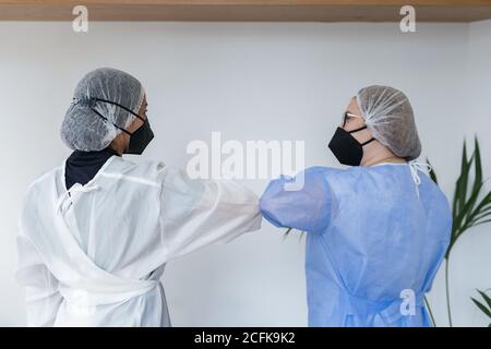 Rückansicht der weiblichen medizinischen Arbeiter in Uniform und schützend Masken begrüßen einander mit Ellenbogen Beule in der Klinik während Coronavirus-Pandemie Stockfoto