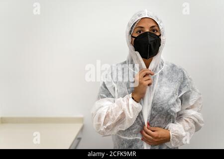 Ärztin, die Schutzanzug mit Gesichtsmaske aufsetzt Und Schutzkappe bei der Vorbereitung auf die Arbeit während der Coronavirus-Pandemie Stockfoto