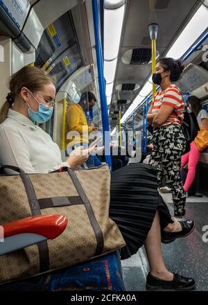 Passagiere im Londoner U-Bahn-Wagen tragen Gesichtsbezüge und versuchen, soziale Distanzierung zu üben. Stockfoto