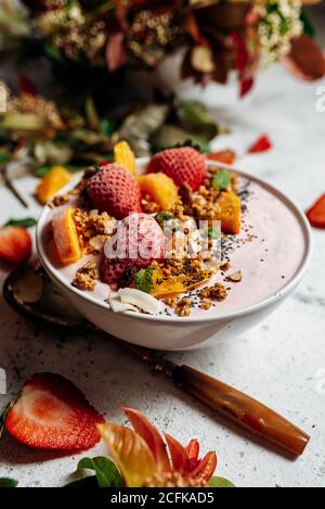 Draufsicht auf nahrhafte Smoothie Schüssel mit Erdbeeren und Nüssen Auf dem Tisch mit grüner Pflanze und verschiedenen Früchten angeordnet Stockfoto