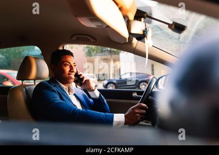 Seitenansicht des erfolgreichen jungen afroamerikanischen männlichen Unternehmers in Elegante formelle Anzug reden auf Handy, während Auto fahren An der City Street Stockfoto