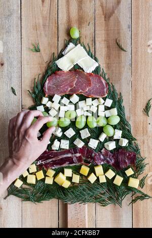 Draufsicht der Hand Platzierung einer Komposition mit sortiert Vorspeisen in Form von Weihnachtsbaum auf Holzhintergrund Stockfoto