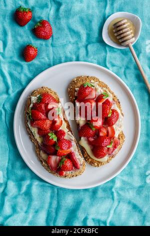 Draufsicht auf leckere süße Brot Toasts mit frisch gehackt Erdbeeren und Honig werden auf dem Teller auf blauer Tischdecke serviert Stockfoto