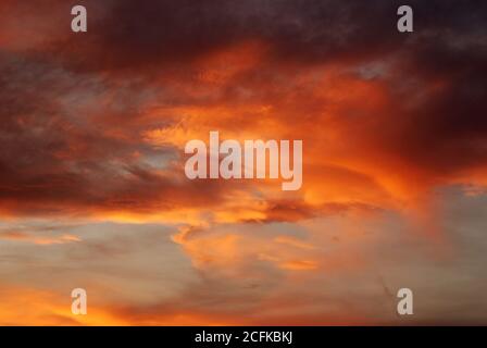 Dunkelblutroter Himmel Hintergrund. Dramatische schwere Wolken mit dem Hauch der Sonne bei Sonnenuntergang. Viele Orange Töne und Muster von Wolken. Stockfoto