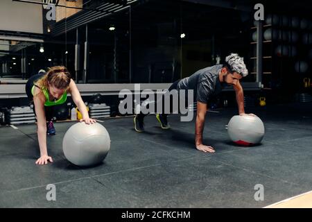 Volle Länge der starken bestimmt athletischen Mann und Frau, die Plank-Übung mit einer Hand mit Medizinball während des Trainings im Fitnessstudio Stockfoto