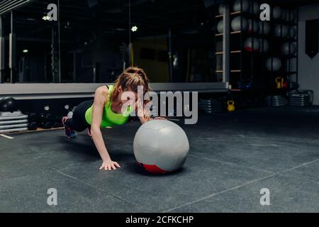 Die ganze Länge der starken, entschlossenen, athletischen Frau, die während des Trainings im Fitnessstudio mit einer Hand mit Medizinball trainiert Stockfoto