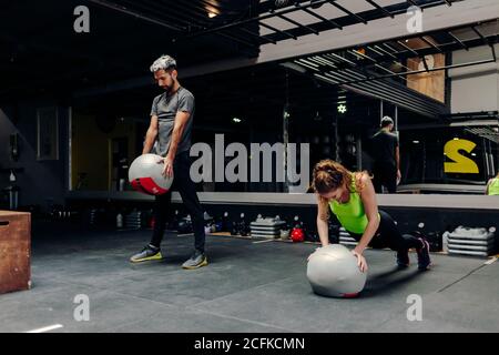 Ganzkörper junge aktive sportliche männliche und weibliche tun Übungen Mit Medizinbällen beim Training im modernen Fitnesscenter Stockfoto