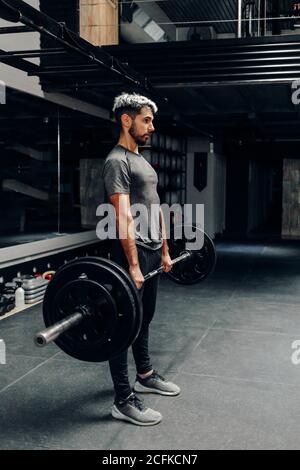 Ganzkörper-Seitenansicht des konzentrierten jungen bärtigen männlichen Athleten Hebe schwere Langhantel während intensivem Training im modernen Sportclub Stockfoto