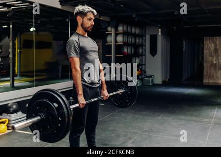 Ganzkörper-Seitenansicht des konzentrierten jungen bärtigen männlichen Athleten Hebe schwere Langhantel während intensivem Training im modernen Sportclub Stockfoto