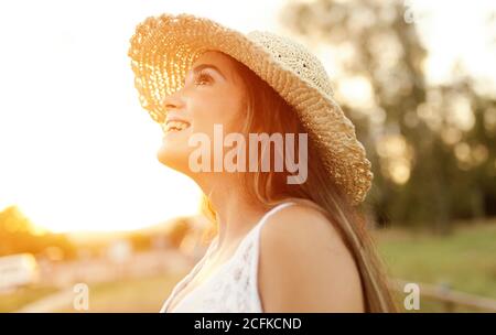 Seitenansicht des Inhalts Weibchen in Sonnenhut stehend auf der Wiese Bei Sonnenuntergang und wegschauen Stockfoto