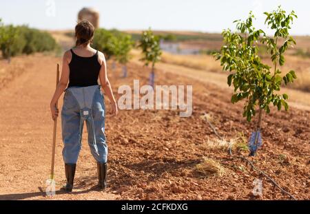 Rückansicht einer unerkennbaren Bäuerin in Sonnenhut mit Rechen Auf dem Boden des Feldes während der Arbeit im Dorf im Sommer Stockfoto