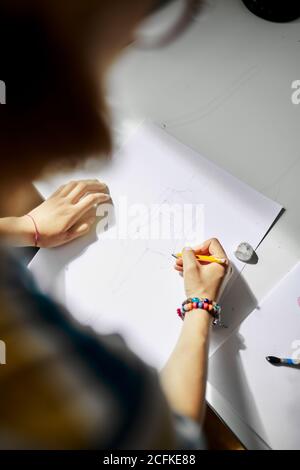 Anonyme kreative Frau, die mit Skizze und Bleistift am Tisch steht, während sie an einem Projekt arbeitet Stockfoto