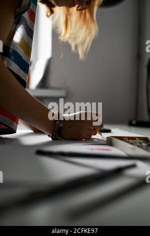 Anonyme kreative Frau, die mit Skizze und Bleistift am Tisch steht, während sie an einem Projekt arbeitet Stockfoto