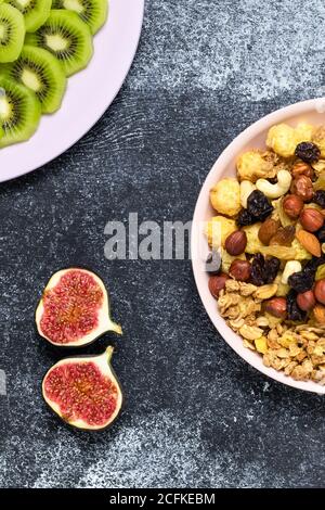 Frische Feigen, Kiwi-Scheiben und Frühstückszerealien, Müsli mit Rosinen und Nüssen. Eine Schüssel trocken gerollter Hafer auf einem dunklen Brett. Haferflocken-Snack. Stillleben. Fla Stockfoto